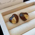 Nahaufnahme von braunen Herz-Ohrsteckern mit goldenem Blatt-Detail in einer Schmuckbox. - Herz Blatt Stil / Braun