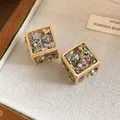 Détail macro de boucles d'oreilles cubes dorées élégantes avec éclats de nacre colorés. - Style Géométrique 3D / Pack de 1 paire / Or-Vert
