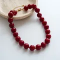 Macro view of large deep red beaded necklace with adjustable gold clasp and chain. - Red