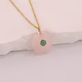 Close-up of a hexagonal pink natural stone pendant with a green inlaid gem on gold chain. - Rose Quartz
