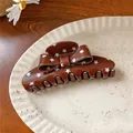Close-up of brown acrylic bow hair claw clip with white star patterns on a plate - Coffee Star Claw Clip