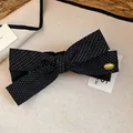 Dettaglio di un fermaglio per capelli vintage a fiocco in tessuto nero a pois con badge oro - Morsetto girevole / pois neri