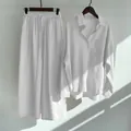 Detailed view of white cotton linen shirt and wide-leg pants set hanging on a wall - White