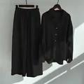 Full view of black cotton linen shirt and wide-leg trousers hanging set on plain wall - Black