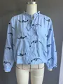 Detailansicht der hellblauen Bluse mit Stickerei und Rüschenkragen auf einer Schaufensterpuppe - XS / Oberteile / Stil 2