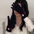 Close-up detail of navy knit gloves with red trim and white logo label worn on hand - One Size / Navy Blue