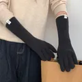Close-up detail of black ribbed knit gloves with beige contrast trim and label - One Size / Black