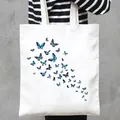 Close-up of a white canvas tote bag with blue butterfly print pattern held by a person. - Flying Blue Butterflies Style (21)