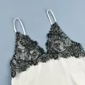 Detail view of delicate black floral lace stitching on a creamy white satin camisole top. - S / Tops / Apricot