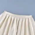 Detailed macro view of cream satin pleated lantern pants featuring elegant texture and waistband - S / Bottoms / Apricot