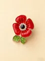 Gros plan d'une broche coquelicot en émail rouge avec cristaux verts et blancs étincelants - Or
