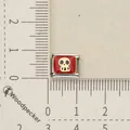 Detailed close-up of a red and gold skull Italian charm link on a measuring scale for DIY bracelets - Skull Pattern (4)