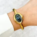 Close-up view of an elegant ladies gold bangle watch with black oval dial worn on wrist - Oval Dial Black Bangle Style / Gold