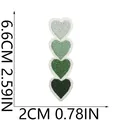 Dettaglio di quattro toppe ricamate a cuore verde con dimensioni per abbigliamento. - 6.6x2cm