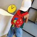 Toddler wearing a cute red cartoon dinosaur backpack with 3D spikes for kindergarten - Red