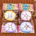 Detail of four colorful Pinch Family squishy toys displayed on a brown woven tray. - Strawberry Cake / Random Color