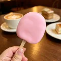 Dettaglio di uno squishy a forma di ghiacciolo rosa tenuto in mano in un caffè accogliente - Stile gelato croccante / 1 Pezzo / Rosa