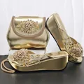 Detailansicht der goldenen Metallic-Keilsandaletten und passenden Clutch mit Blumenschmuck. - Gold