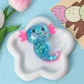 Detail eines blauen Glitzer-Axolotl-Squishy-Spielzeugs auf einem weißen Sternenteller. - 3D Stil (RYNN-1) / Blau
