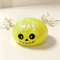 Juguete squishy de Halloween amarillo con purpurina y cara de fantasma sobre blanco - Calavera