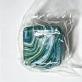 Close-up view of a blue marble pattern square squishy toy in its clear plastic packaging bag - Square Style / Green