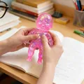 Transparente rosa Glitzer-Puppen-Anti-Stress-Spielzeug, das über ein Notizbuch gehalten wird. - 11cm Size / Irisierendes Rosa