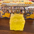 Detailweergave van een geel kaas-squishy-speeltje met de winkelverpakking erbij. - Driekleurige Kaas - Geel