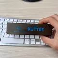 Brown butter-style slow rebound squishy stress relief toy being held over a keyboard - Butter Chocolate Stick / Tan