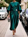 Detalle de un elegante vestido de satén verde esmeralda con broche floral brillante. - Verde