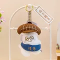 Primer plano de un adorable llavero de peluche blanco con gafas y gorro marrón - Oreja de mar (Ambicioso) / Blanco / Aprox 10cm