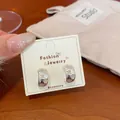 Silver-tone hoop earrings with enamel star patterns on a display card. - Maillard Star Hoop Earrings (MLA3)
