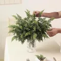 Close-up of hands arranging artificial cedar branches in a crystal vase for decor - Set of 12 / Green