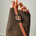 Detalle de un elegante reloj de cuarzo ovalado para mujer con correa de cuero marron claro - Correa de Cuero / Naranja