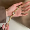 Détail d'une montre-bracelet dorée vintage avec d'élégantes incrustations de pierres vertes. - Vert Vanille Avec Cadran Blanc Et Cadre Doré