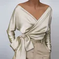 Close-up view of an elegant champagne satin V-neck wrap blouse featuring a stylish bow tie waist - S / Tops / Apricot