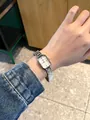 Close-up view of a chic silver square women's watch worn on wrist with denim. - Silver White