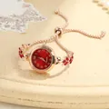 Macro view of a feminine rose gold bracelet watch featuring red clover crystal accents - Red