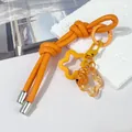 Primer plano de un llavero creativo de cuerda de cuero naranja con dijes de flores y cascabel - Doble nudo / Naranja