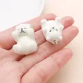 Primer plano de dos dijes de osos blancos flocados sostenidos en la mano para joyería DIY - Oso polar / 28x17x15mm / Blanco