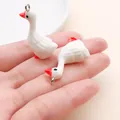 Detailed close-up view of two small white goose charms held in a palm for DIY jewelry craft - White Resin 3D Goose (27562) / 1 Piece (33x12x20mm) / White