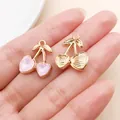 Detail view of gold cherry charms featuring pink heart rhinestones on a hand. - KC Gold Pink Heart Rhinestone Cherry (Asymmetric)