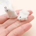 Gros plan de mini breloques lapin en peluche blanche pour bijoux DIY sur une paume - Lapin à Longues Oreilles Assis Latéralement (27679) / 1 Pièce (23x12x21mm) / Blanc