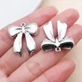 Primer plano detallado de colgantes de lazo plateado vintage para joyería DIY. - 26996 - 1 ud. 24,5x22mm 4g lazo de aleación de zinc plata antigua