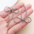 Primer plano de colgantes de lazo en plata antigua para crear collares de DIY - Lazo de Cuerda Larga (26998) / 1 Pieza (43x36mm) / Plata antigua