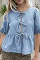 Dettaglio di una camicia in denim azzurro con tre fiocchi frontali e maniche a sbuffo. - Taglia S / Top / Azzurro