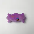 Detalle de un juguete de peluche morado con forma de caramelo y bordado Sugar decorativo. - Caramelo / Púrpura