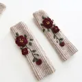 Close-up of beige knitted arm warmers with red floral embroidery and green leaves. - Floral Arm Sleeves