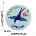 Light blue embroidered bird patch with flower and Spring text, 5.8cm diameter - SPRING Swallow Blue Base (Style 16)