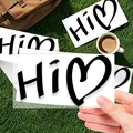 Close-up of a hand holding a transparent heart Hi sticker on a green grass background - c473 / 15cm x 8.1cm