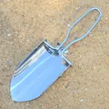 Dettaglio di una mini pala da giardino pieghevole in acciaio inox su fondo sabbioso. - colore naturale dell'acciaio